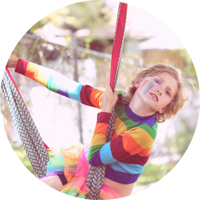 A child wearing rainbow face paint and clothing swings from a hammock